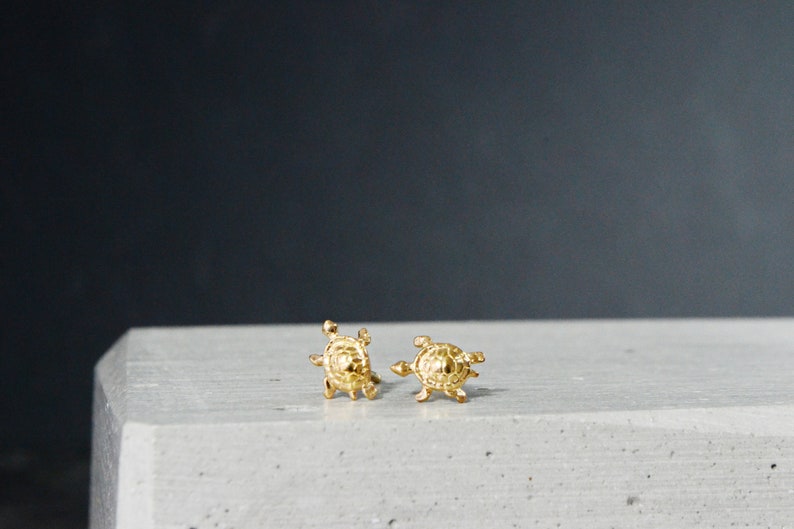 May include: A pair of gold turtle stud earrings. The earrings are small and delicate, and they are perfect for adding a touch of whimsy to any outfit.