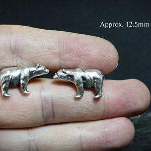 Op de afbeelding: Twee zilveren berenbeeldjes die elkaar aankijken. Ongeveer 12,5 mm x 22 mm.