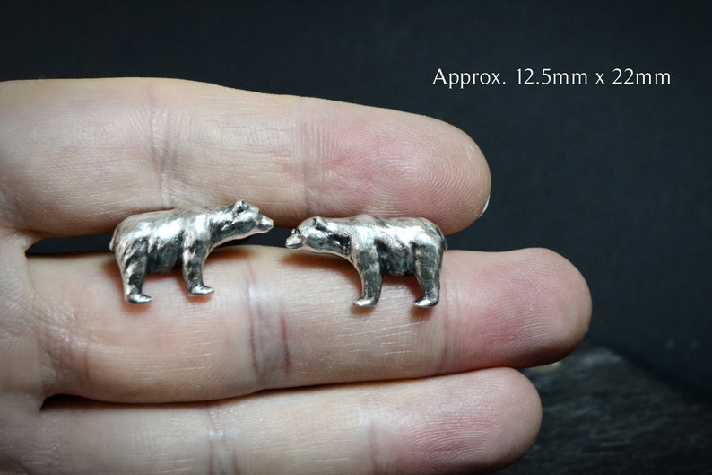 Op de afbeelding: Twee zilveren berenbeeldjes die elkaar aankijken. Ongeveer 12,5 mm x 22 mm.