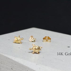 May include: A pair of gold turtle stud earrings. The earrings are made of 14K gold and feature a detailed turtle design. 14K Gold