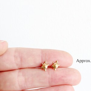 May include: A pair of gold turtle stud earrings. The earrings are approximately 6x8 millimeters in size.