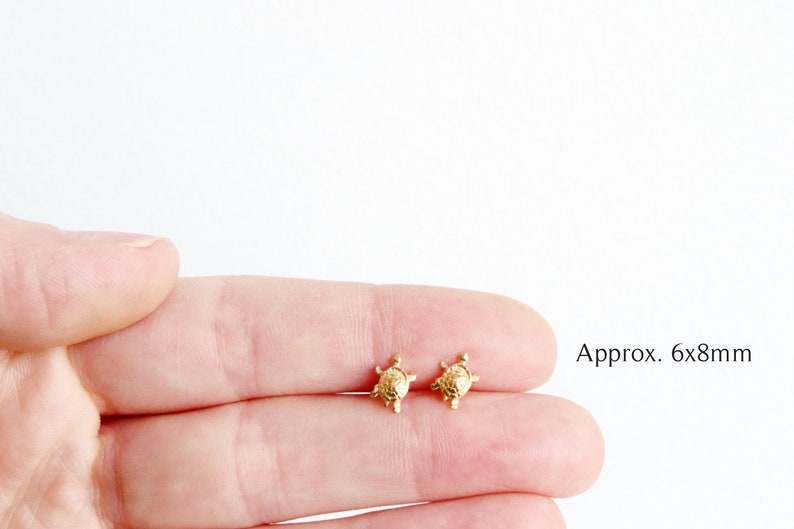 May include: A pair of gold turtle stud earrings. The earrings are approximately 6x8 millimeters in size.