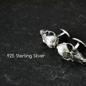 May include: A pair of silver cufflinks shaped like animal skulls. The cufflinks are made of 925 sterling silver.