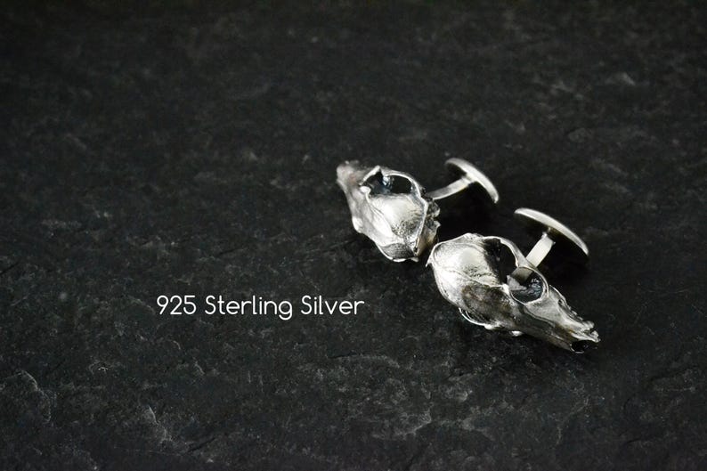 May include: A pair of silver cufflinks shaped like animal skulls. The cufflinks are made of 925 sterling silver.