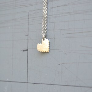 May include: A silver chain necklace with a small, silver, pixelated heart pendant.