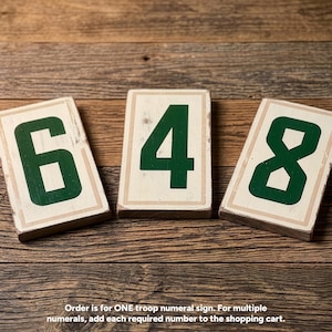 May include: Three rectangular wooden signs featuring the dark green numerals 6, 4, and 8 painted on a cream-colored background with a light brown border. Each sign has a distressed finish and the text: Order is for ONE troop numeral sign.