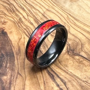 May include: A black and red ring with a red wood inlay. The ring is made of black tungsten carbide and has a polished finish.
