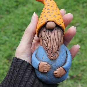 May include: A ceramic gnome figurine with a blue shirt, brown beard, and a yellow hat with brown polka dots.