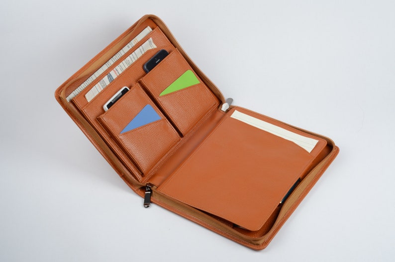 K&ouml;nnte beinhalten: Offenes braunes Leder-Zipper-Portfolio mit mehreren Taschen und einem Notizblock. Die Taschen haben blaue und gr&uuml;ne Akzente.