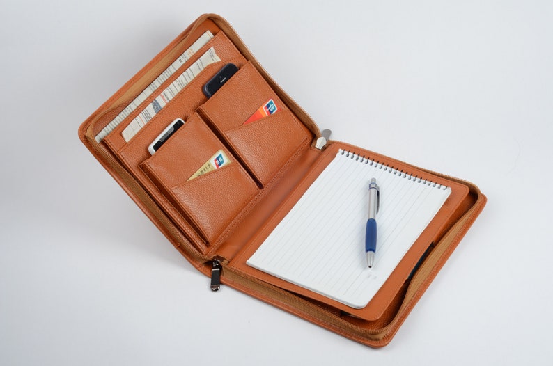 K&ouml;nnte beinhalten: Ein braunes Leder-Zipper-Portfolio mit einem Notizblock, einem Stift und mehreren Taschen f&uuml;r Karten und ein Telefon.