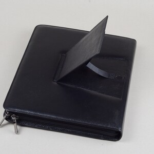 May include: Black leather zippered portfolio with a built-in stand for holding a tablet or phone.
