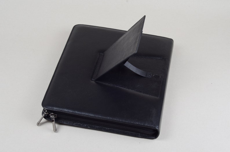 May include: Black leather zippered portfolio with a built-in stand for holding a tablet or phone.