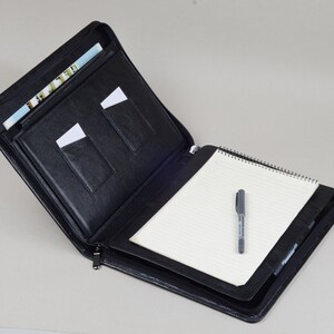 May include: Black leather zippered portfolio with a notepad and pen. The portfolio has multiple pockets for holding cards and documents.