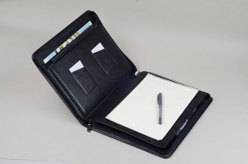 May include: Black leather zippered portfolio with a notepad and pen. The portfolio has multiple pockets for holding cards and documents.