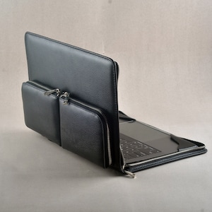 May include: A black leather laptop sleeve with a zipped pocket on the front. The sleeve is open and a laptop is visible inside.