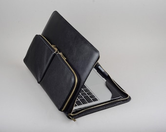 May include: Black leather laptop sleeve with a zipper closure and an additional zippered pocket. The sleeve is open and a laptop is inside.