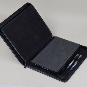 May include: A black leather zippered portfolio case with a gray felt interior. The case is open and has three black pens inside.