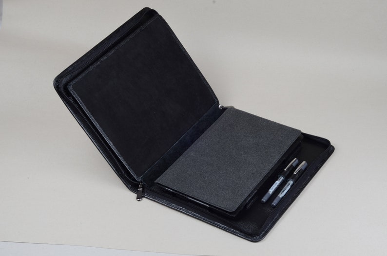 May include: A black leather zippered portfolio case with a gray felt interior. The case is open and has three black pens inside.