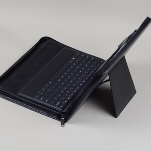 May include: A black leather case with a built-in keyboard and a stand for a tablet or laptop.