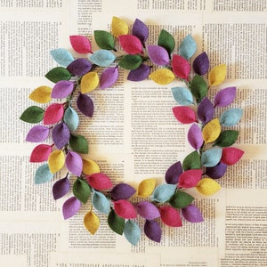 May include: A colorful felt leaf wreath with leaves in shades of pink, yellow, green, purple, and blue. The wreath is arranged in a circular shape, perfect for home decor.