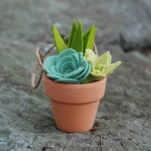 May include: A small terracotta pot with a green felt succulent plant inside. The succulent is made of felt and has a light green and teal color scheme.