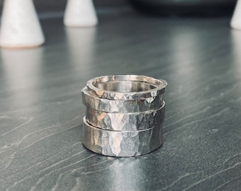 May include: A stack of four silver rings with a hammered texture. The rings are stacked on top of each other, with the largest ring at the bottom and the smallest ring at the top.