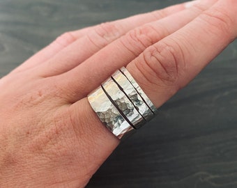 May include: A set of four silver hammered stacking rings worn on a finger.