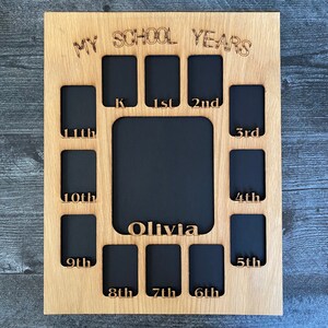 May include: A wooden photo frame with cutouts for pictures, labeled with the years of school, from kindergarten to 12th grade. The frame is labeled "My School Years" and has a space for a name, "Olivia".