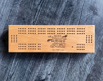 May include: A wooden cribbage board with numerous drilled holes for pegging. The board features the engraved text "the BEST Memories ARE THE ONES WE SHARE with Friends". The board is rectangular and made of light-colored wood.