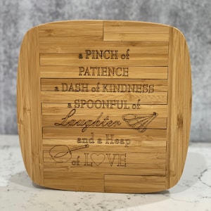 May include: A wooden cutting board with a quote engraved on it: "a pinch of patience, a dash of kindness, a spoonful of laughter, and a heap of love".