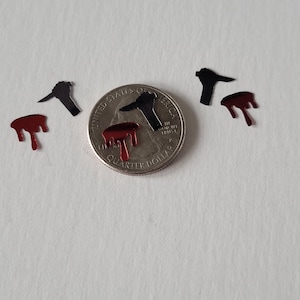 May include: Black and red glitter shapes of a knife and dripping blood. The shapes are about the size of a US quarter.