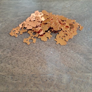 May include: A pile of copper-colored confetti shaped like small bears. The confetti is scattered on a wooden surface.