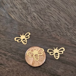 May include: Three gold bee cutouts on a wooden surface. One bee cutout is on top of a US penny with the year 2012.