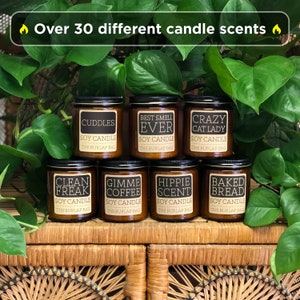 Puede incluir: Una colecci&oacute;n de ocho velas de soja en frascos de vidrio &aacute;mbar con diversos aromas, entre ellos "Cuddles", "Best Smell Ever", "Crazy Cat Lady", "Clean Freak", "Gimme Coffee", "Hippie Scent" y "Baked Bread". Cada vela tiene una etiqueta negra con texto blanco y las palabras "Soy Candle" y "The Burlap Bag".