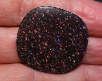 May include: A dark brown opal cabochon with a speckled pattern of iridescent colors, including red, blue, and green.