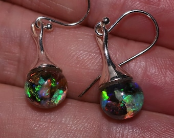 May include: A pair of silver-toned drop earrings. Each earring features a teardrop-shaped, iridescent opal stone. The opals display a vibrant array of colors, including green, blue, and red. The earrings are designed with a simple, elegant hook.