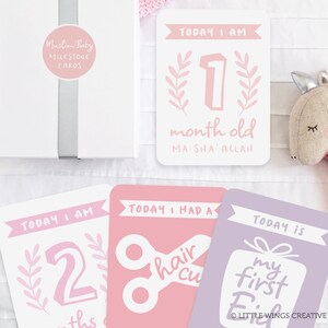 May include: A set of pink and purple milestone cards for a baby. The cards feature illustrations of a number one, a number two, scissors, and a gift box. The text on the cards reads "Today I am 1 month old Ma Sha'Allah", "Today I am 2 months old", "Today I had a hair cut", and "Today is my first Eid".