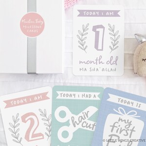 May include: A set of milestone cards for a baby. The cards are white with pink, blue, and green accents. The cards feature text such as "Today I am 1 month old", "Today I had a haircut", and "Today is my first".