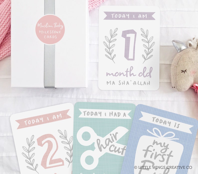 May include: A set of milestone cards for a baby. The cards are white with pink, blue, and green accents. The cards feature text such as "Today I am 1 month old", "Today I had a haircut", and "Today is my first".