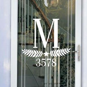 May include: White vinyl decal with a letter M, a star, and two branches of leaves. The number 3578 is below the leaves. The decal is on a glass door with a white frame.
