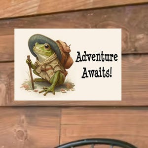 May include: A whimsical illustration of a frog dressed as a hiker, wearing a hat and carrying a backpack and walking stick. The image is on a cream-colored background with the words "Adventure Awaits!" in black text.