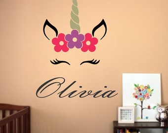 May include: A black unicorn silhouette with a green horn and pink and purple flowers on a beige wall. The name Olivia is written in black cursive below the unicorn.