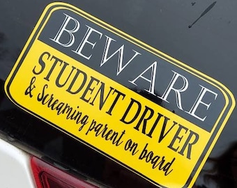 May include: A rectangular car decal with rounded corners featuring a black top section with the white text BEWARE and a yellow bottom section with the black text STUDENT DRIVER and the script text & Screaming parent on board.