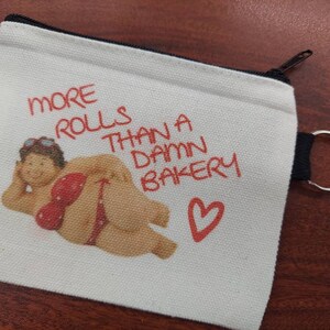 May include: White canvas zippered pouch with a black zipper and a black ring attached. The pouch has a red heart and the text "More rolls than a damn bakery". A cartoon image of a woman in a red bikini is on the pouch.