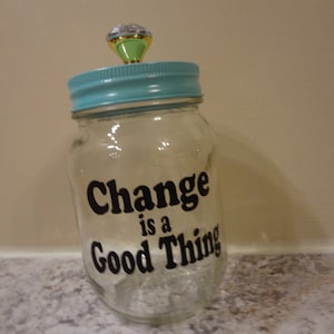 May include: A clear glass jar with a blue lid and a crystal knob. The jar has a black vinyl sticker that reads "Change is a Good Thing".