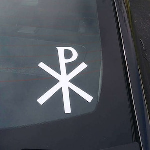 May include: White vinyl sticker of the Chi Rho symbol, a Christian symbol, on a black car window.