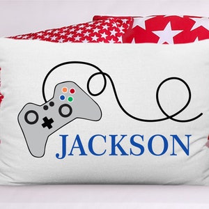 May include: White pillow with a gray video game controller and a black cord. The name "JACKSON" is written in blue letters below the controller.