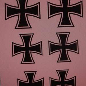 May include: Six black iron crosses with white outlines on a pink background.