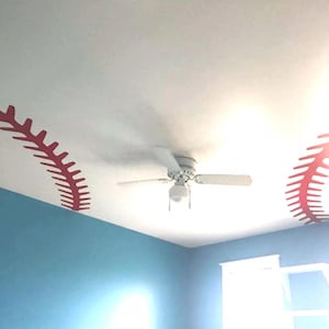 May include: A white ceiling fan with red baseball stitching decals on the ceiling. The ceiling is painted white and the walls are painted blue.