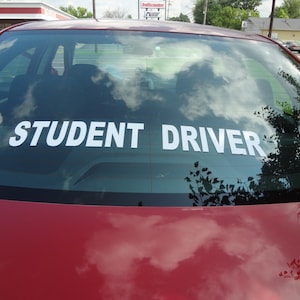 May include: A red car with a white "STUDENT DRIVER" sticker on the rear window.